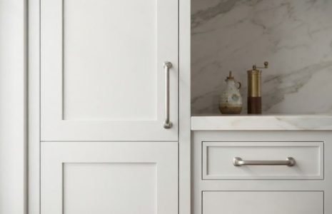 White kitchen cabinetry with marble countertop and brass faucet, an olive oil bottle and pepper grinder on the counter nearby